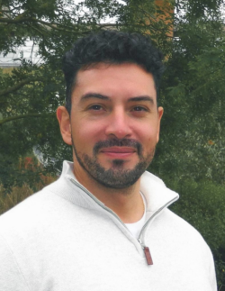 Headshot of Dr Roberto Mansilla. Roberto stands in front of trees.